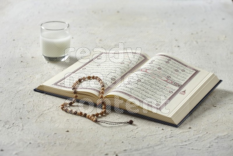 Quran with dates, prayer beads and different drinks all placed on textured white background