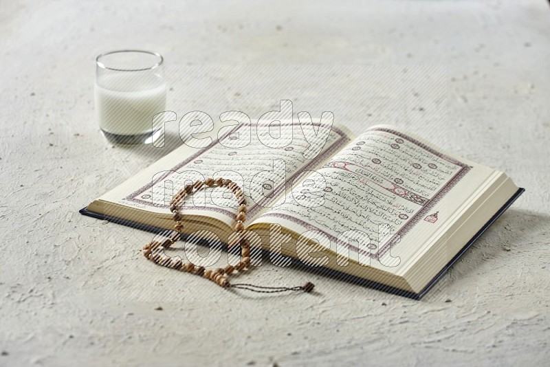 Quran with dates, prayer beads and different drinks on textured white background