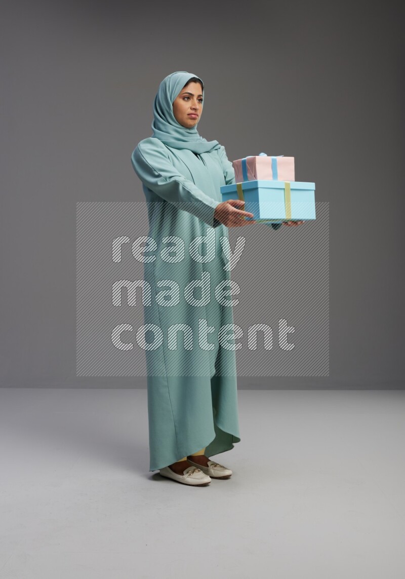 Saudi Woman wearing Abaya standing holding gift box on Gray background