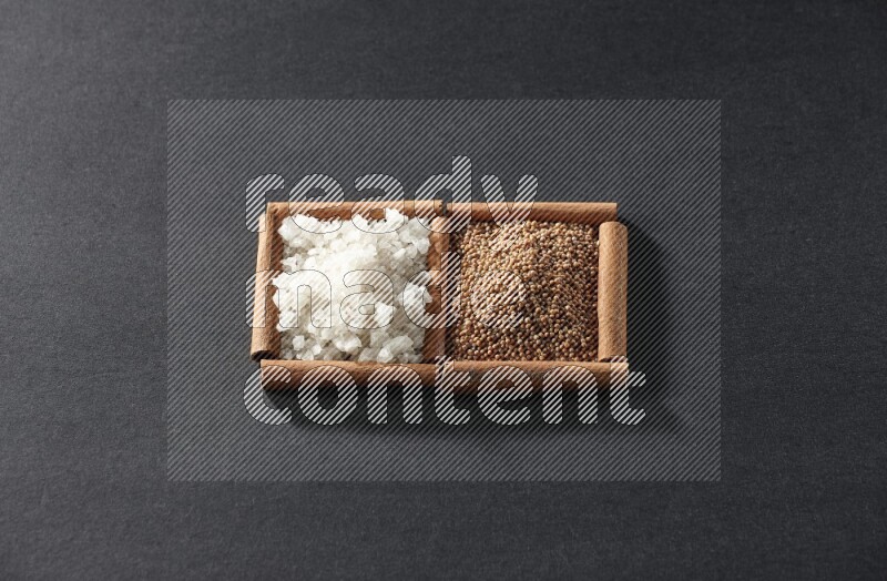 مربعان من أعواد القرفة ممتلئان بحبوب الخردل والملح الأبيض علي خلفية سوداء