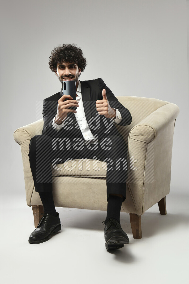 A man wearing formal sitting on a chair shooting with his phone on white background