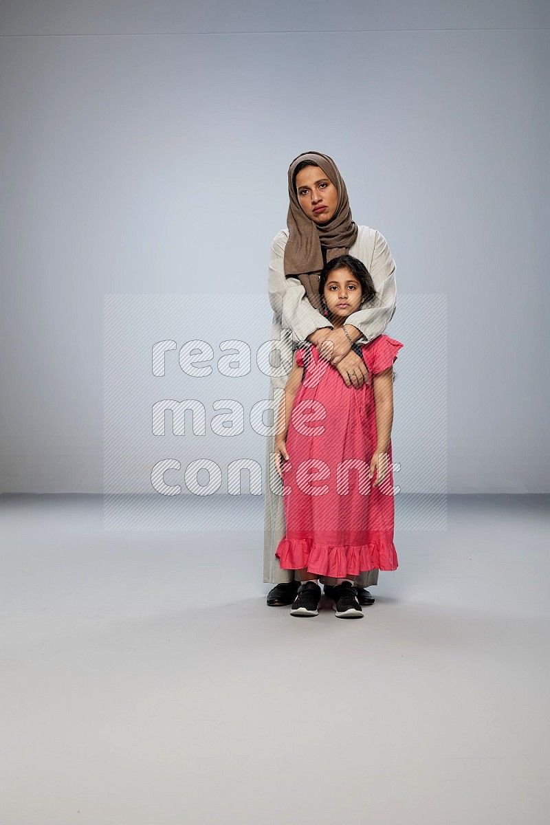 A girl and her mother interacting with the camera on gray background