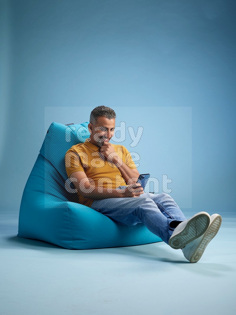 A man sitting on a blue beanbag and texting on phone