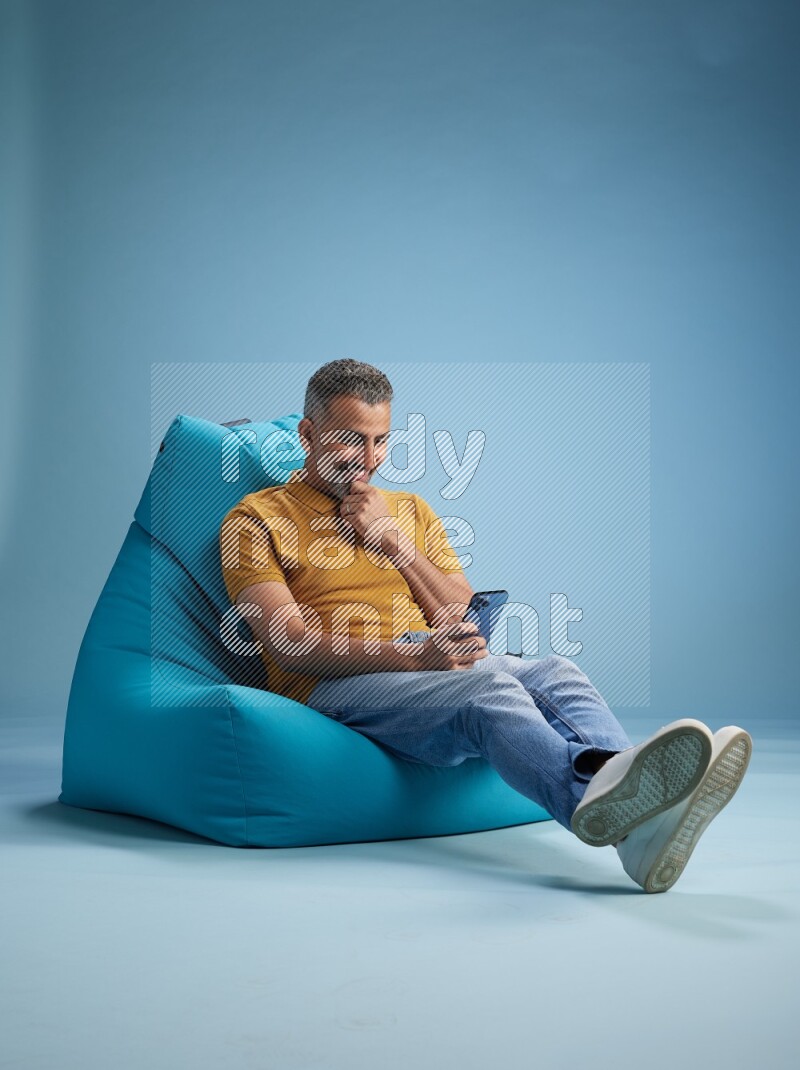 A man sitting on a blue beanbag and texting on phone