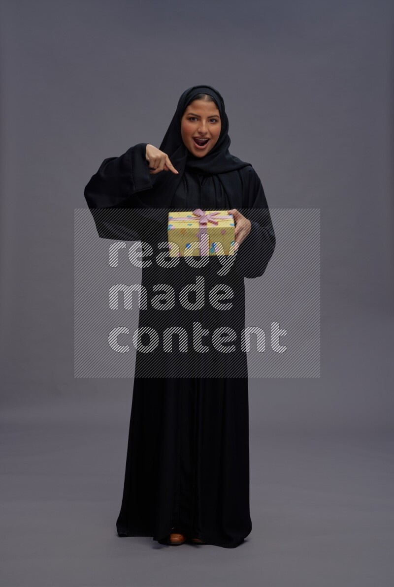 Saudi woman wearing Abaya standing holding gift box on gray background