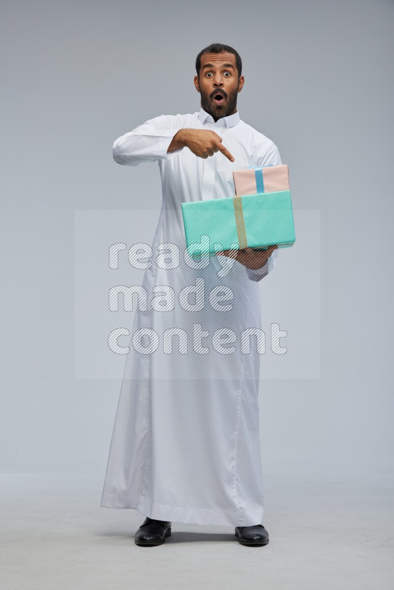 Saudi man Wearing thob standing holding gift box on Gray background