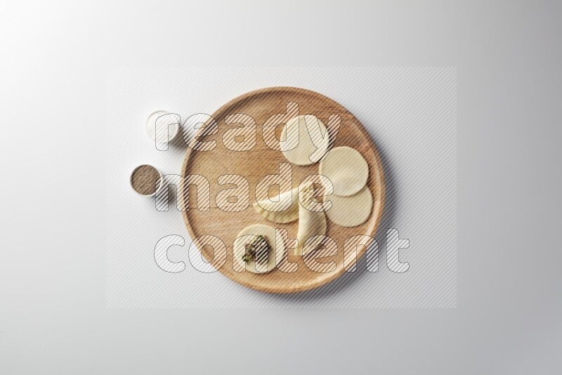 two closed sambosas and one open sambosa filled with meat while salt and black pepper aside in a wooden dish on a white background