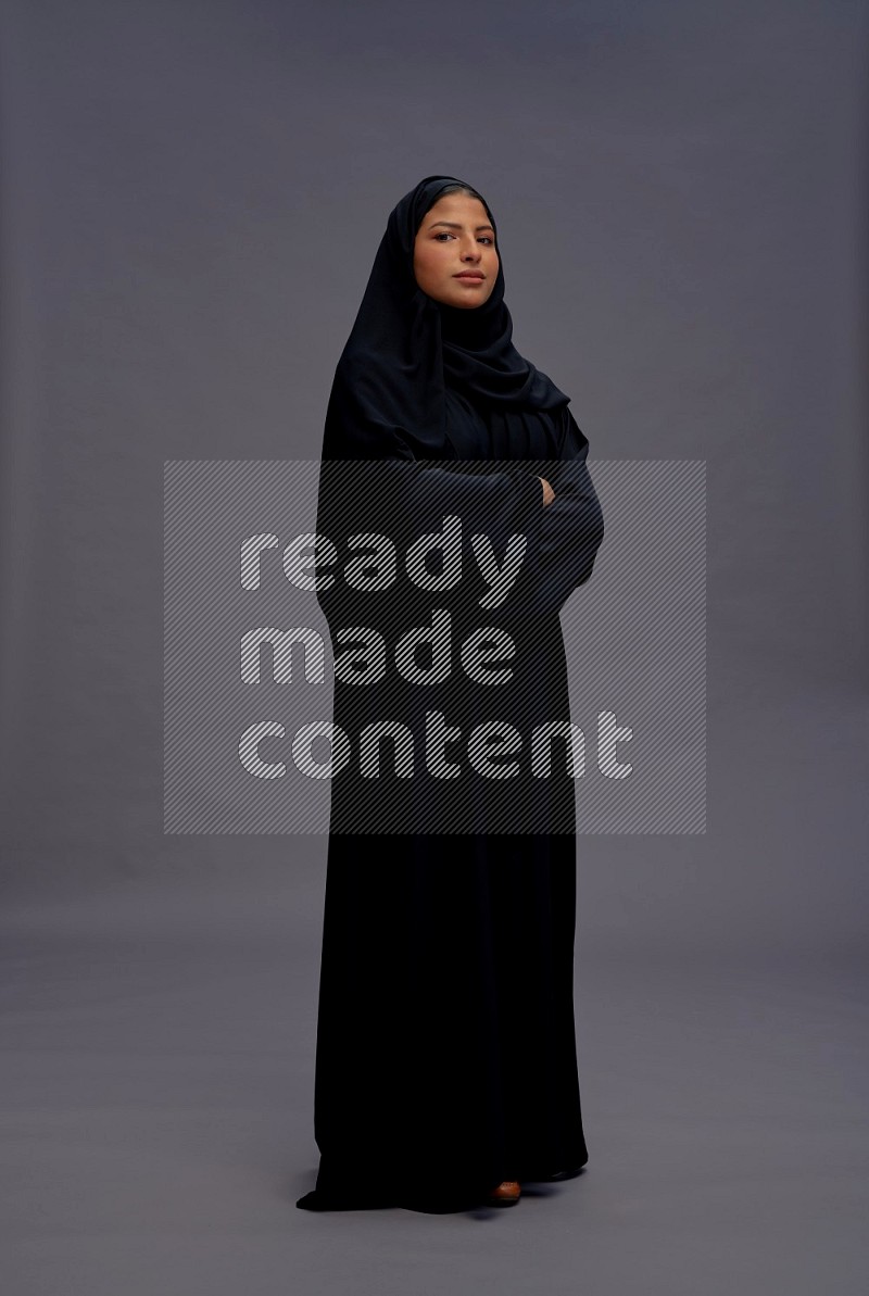 Saudi woman wearing Abaya standing with crossed arms on gray background