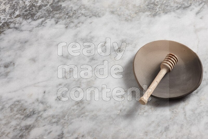 Multicolored pottery plate with wooden honey dipper in it on grey marble background