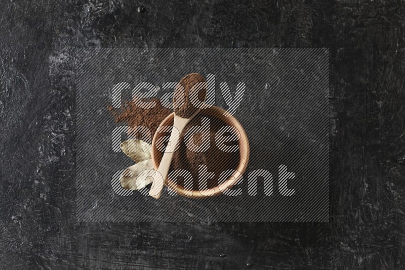 وعاء خشبي وملعقة خشبية ممتلئان ببودرة القرنفل مع أوراق الغار على خلفية سوداء