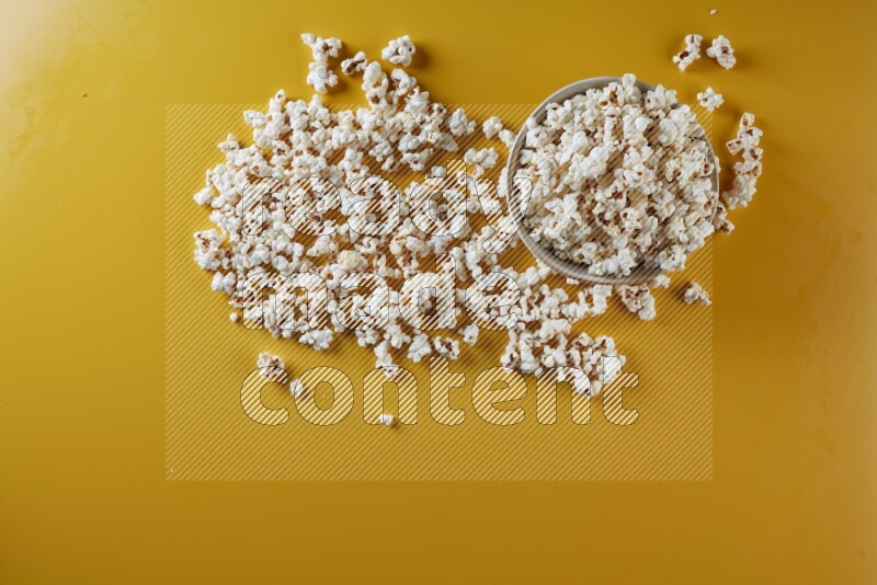 A white pottery bowl full of popcorn with popcorn beside it on a yellow background in different angles