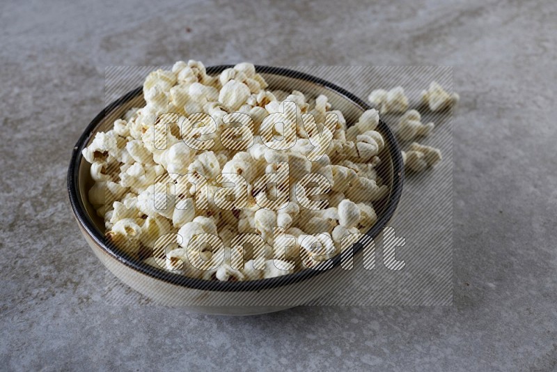 popcorn in a multi-colored pottery bowl on a grey textured countertop