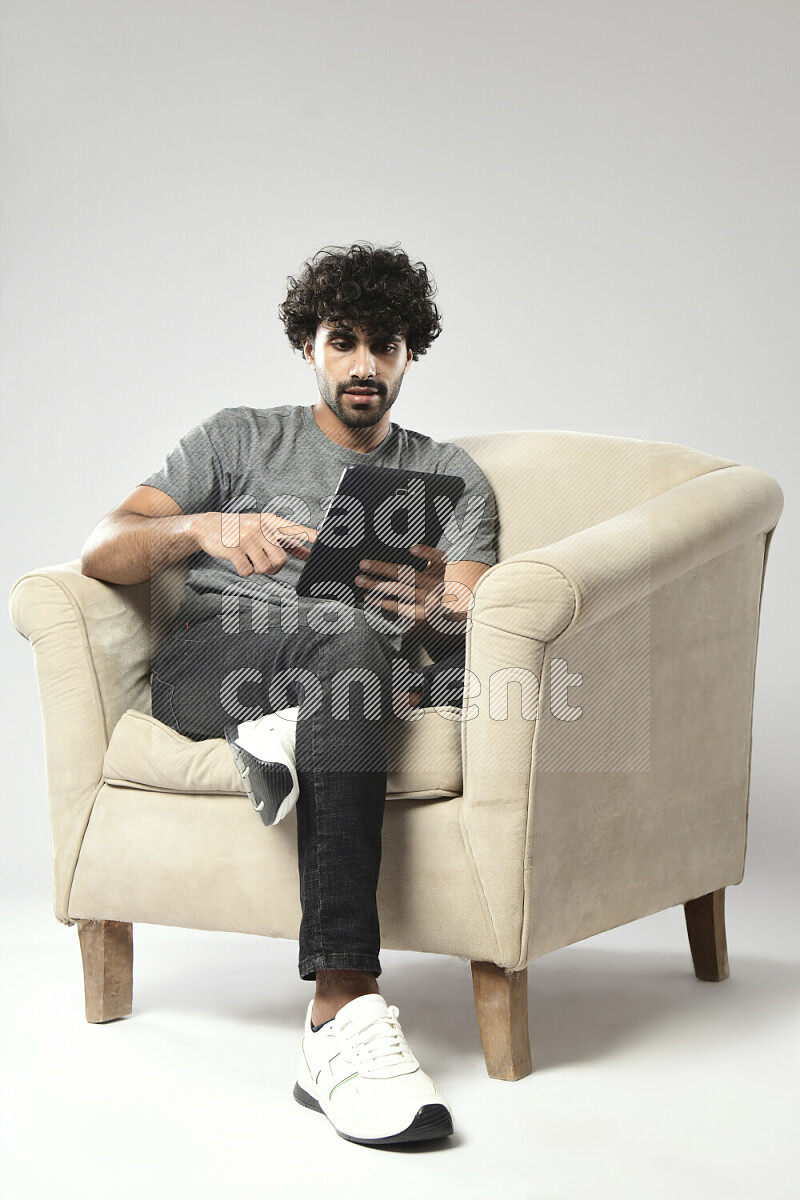 رجل يرتدي ملابس كاجوال يجلس علي كرسي و يتصفح تابلت علي خلفية بيضاء