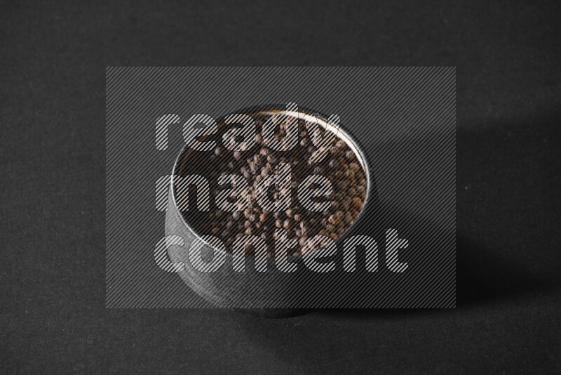 A black pottery bowl full of black pepper beads on black flooring