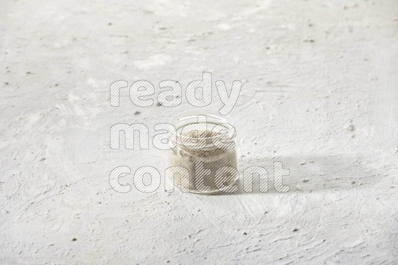 A glass jar full of white pepper powder on textured white flooring