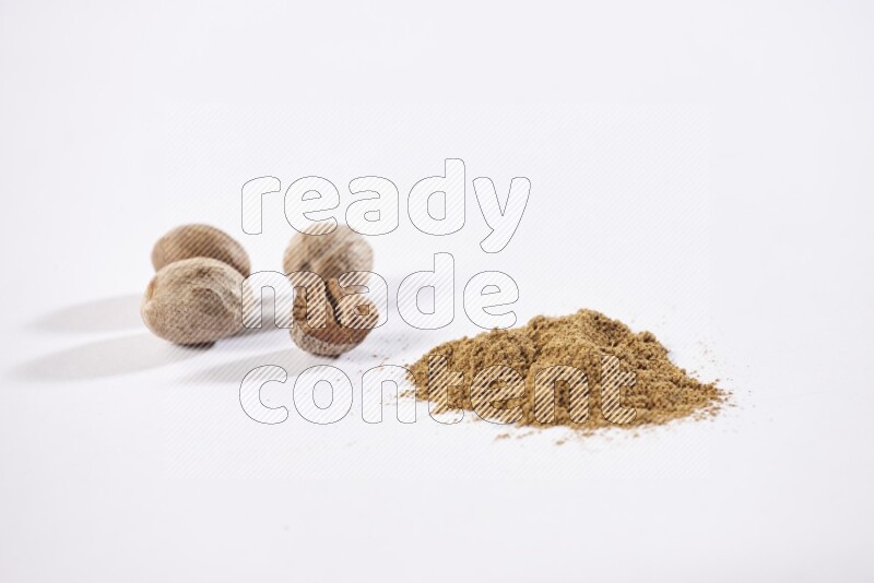 Nutmeg whole seeds with nutmeg powder beside it on a white flooring