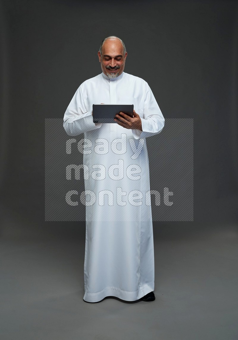 Saudi man without shomag Standing working on tablet on gray background