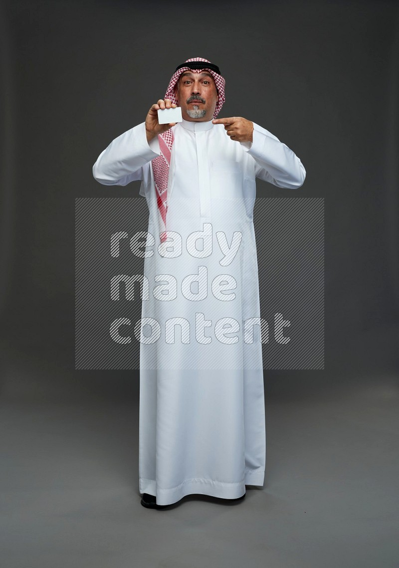 Saudi man with shomag Standing holding ATM card on gray background