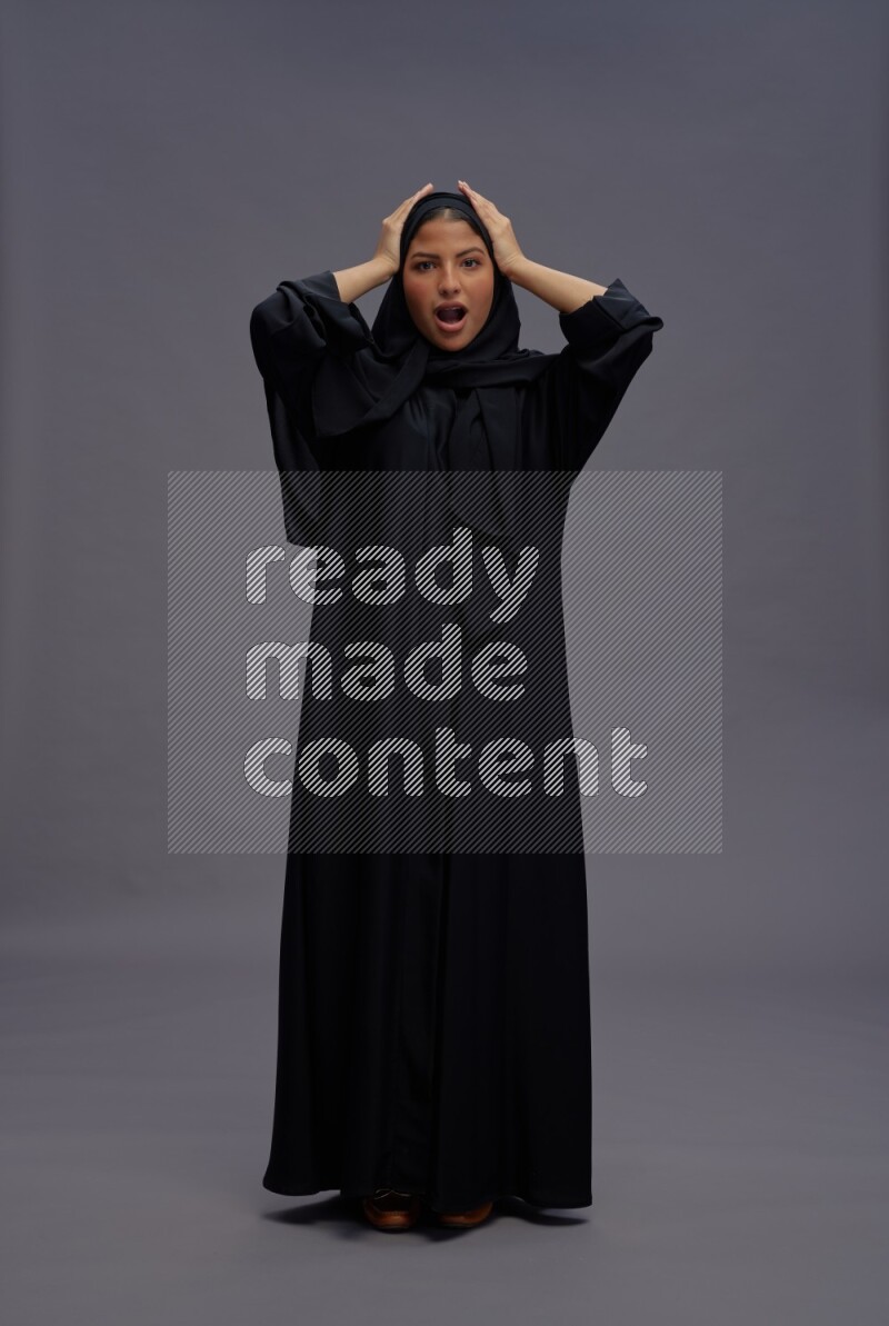 Saudi woman wearing Abaya standing hands behind head on gray background
