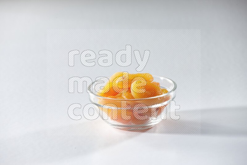 A glass bowl full of dried apricots on a white background in different angles