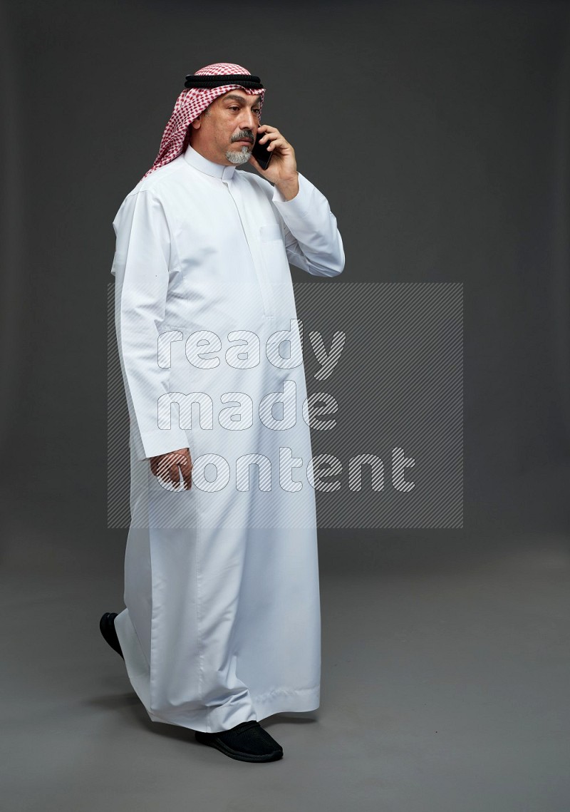 Saudi man with shomag Standing talking on phone on gray background