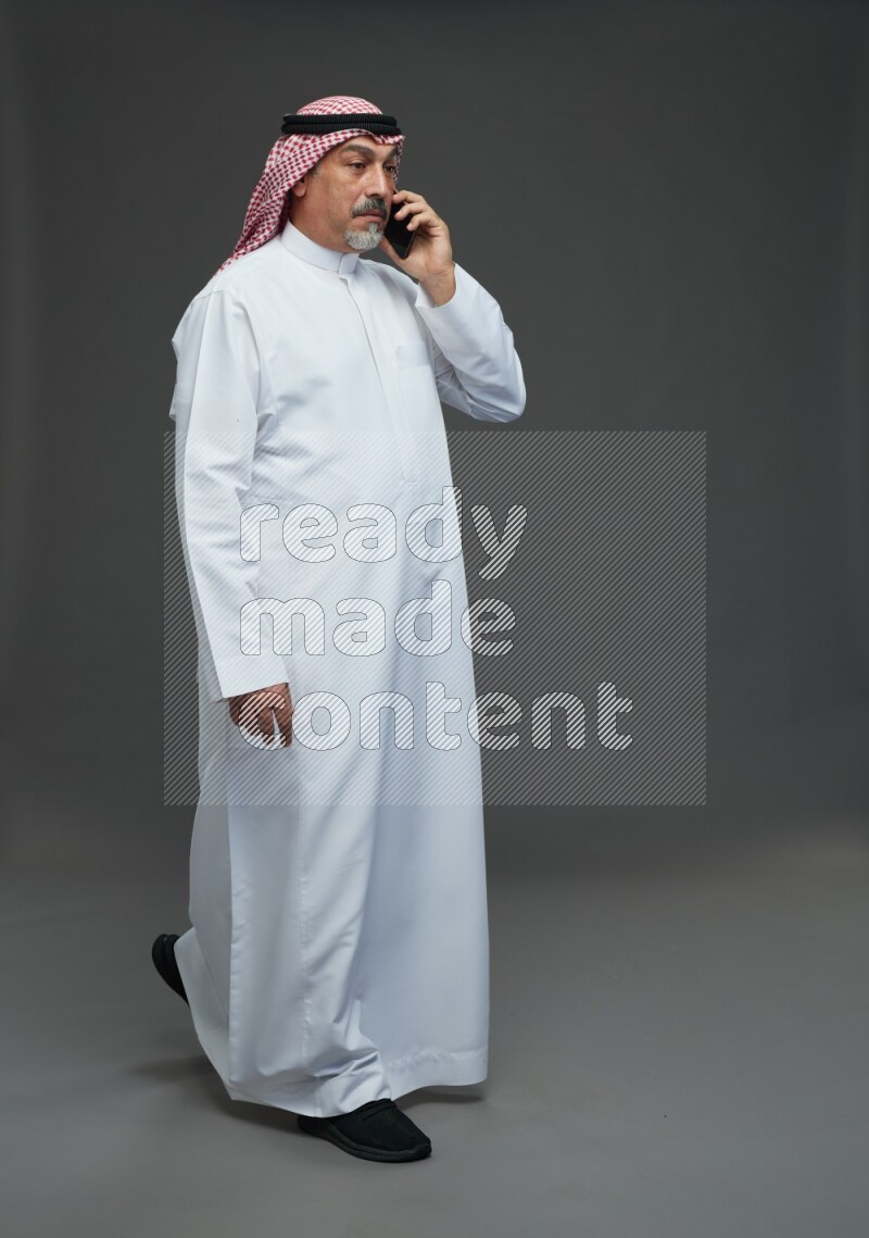 Saudi man with shomag Standing talking on phone on gray background
