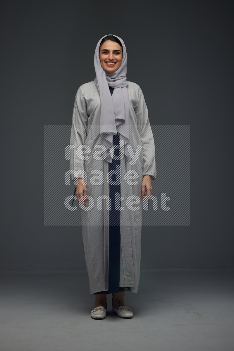 A Saudi woman wearing a light gray Abaya and head scarf standing and making multi poses eye level on a grey background