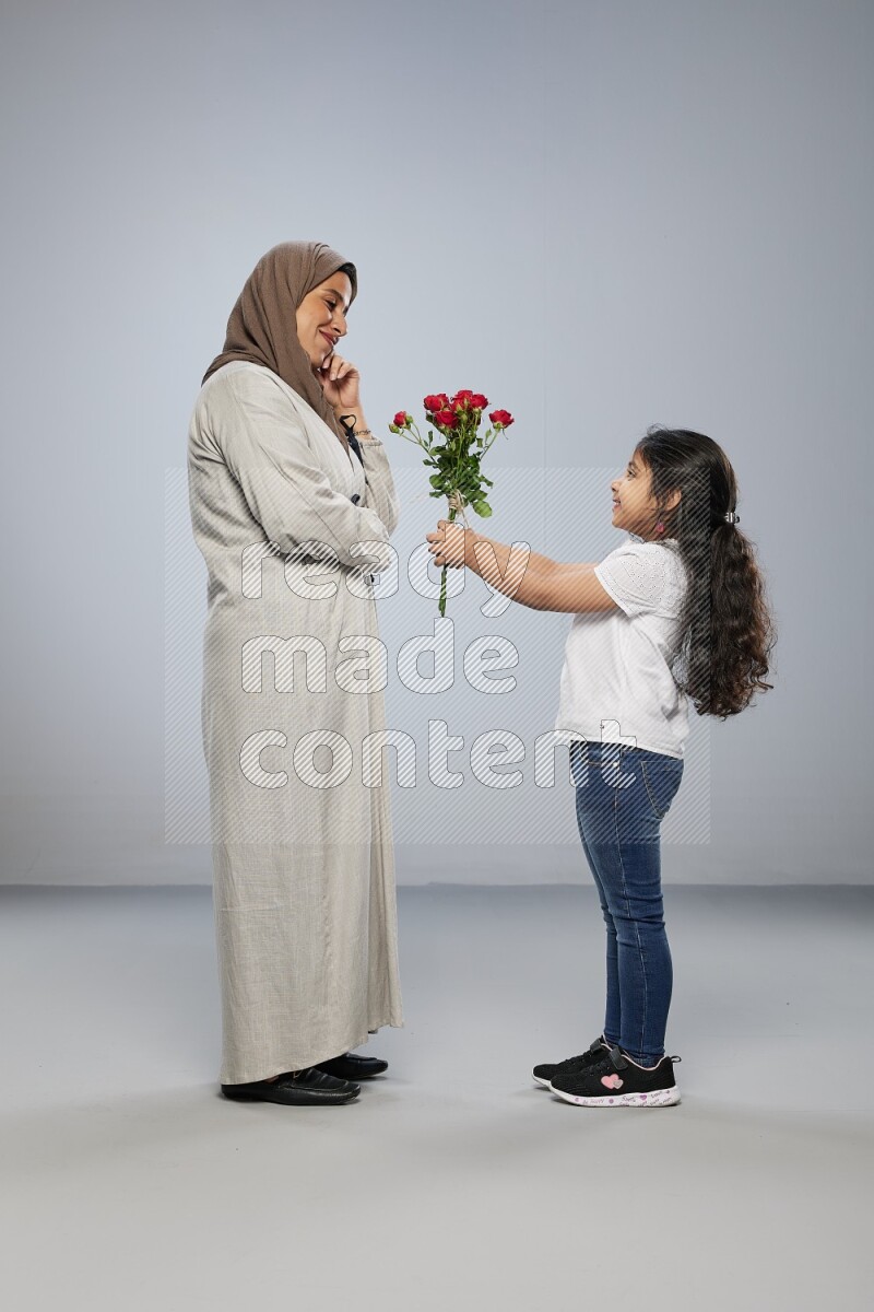 A girl standing giving flowers to her mother on gray background