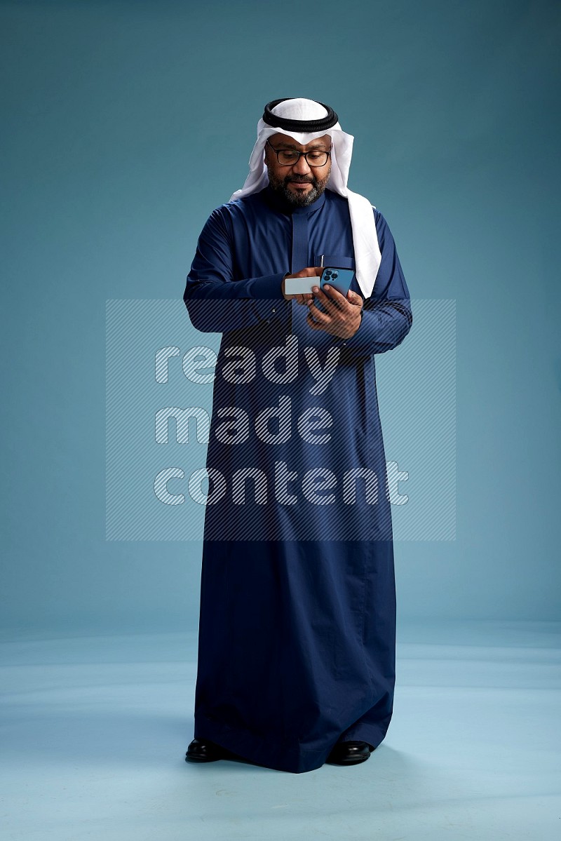 Saudi Man with shimag Standing holding ATM card while talking on phone on blue background