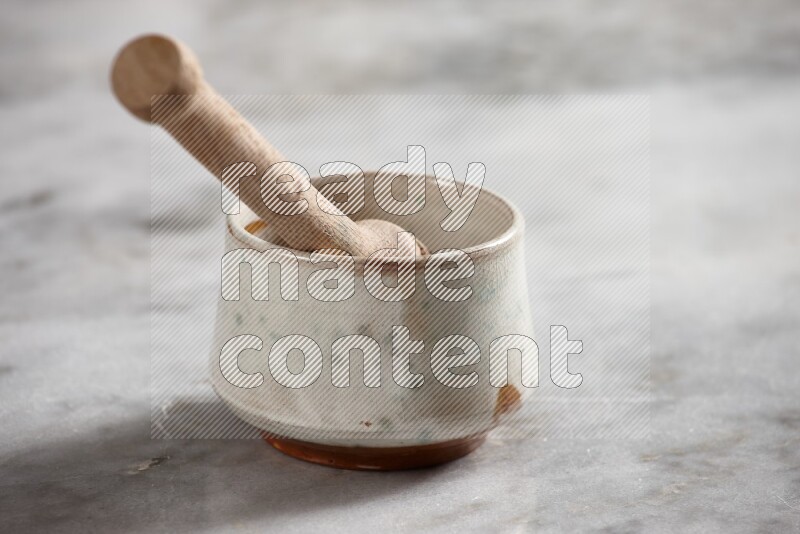Multicolored pottery bowl with wooden honey dipper in it on grey marble background