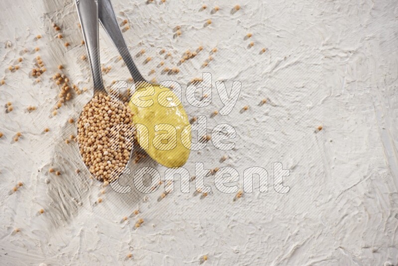 Two metal spoons, one filled with mustard seeds and the other with mustard paste on white background