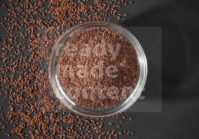 وعاء زجاجي ممتلئ ببذور حب الرشاد محاط بالبذور على أرضية سوداء