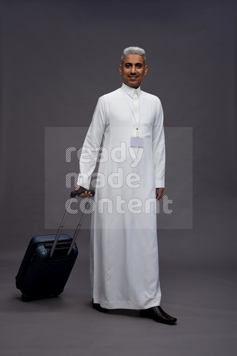 Saudi man wearing thob with neck strap employee badge standing holding bag on gray background