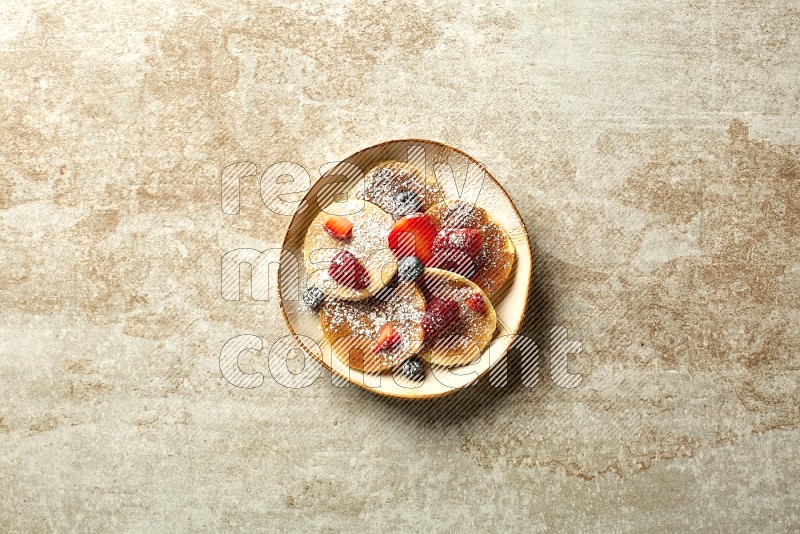 Five stacked mixed berries mini pancakes in an irregular plate on beige background