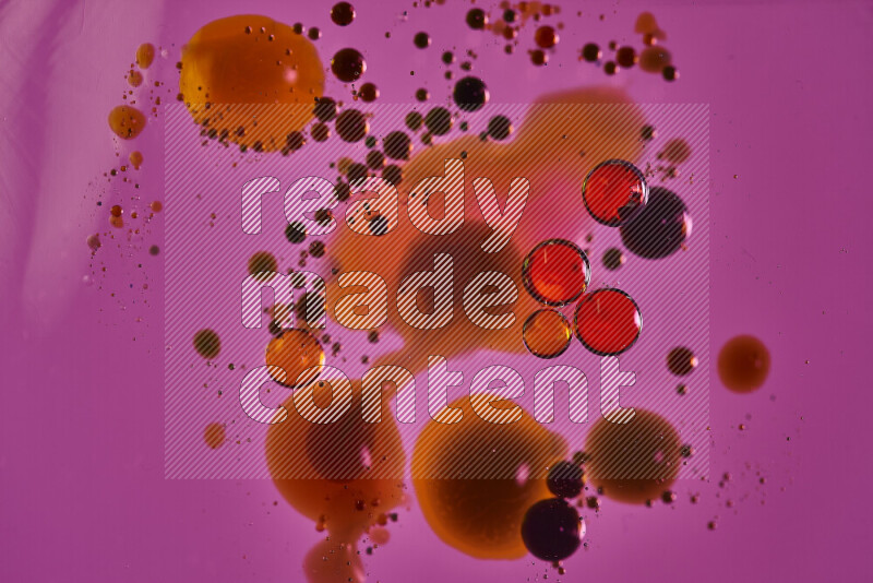 Close-ups of abstract red, blue and yellow watercolor drops on oil Surface on pink background