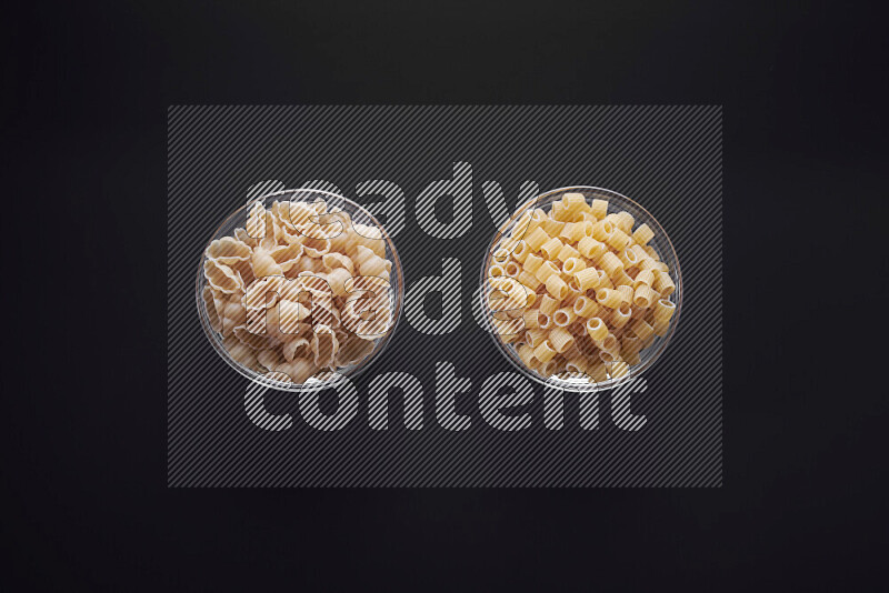 Different pasta types in glass bowls on black background