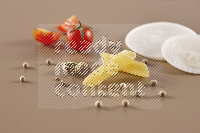 Raw pasta with different ingredients such as cherry tomatoes, garlic, onions, red chilis, black pepper, white pepper, bay laurel leaves, rosemary and cardamom on beige background