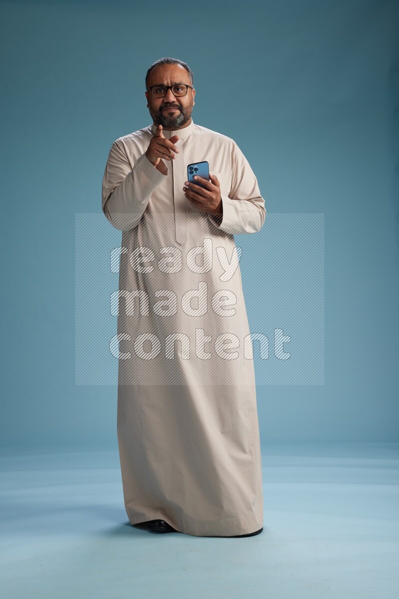 Saudi Man without shimag Standing texting on phone on blue background