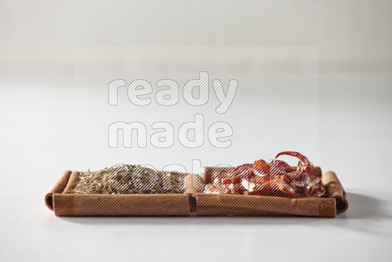 مربعان من أعواد القرفة ممتلئان بالفلفل الحار المجفف وحبوب الكمون علي خلفية بيضاء