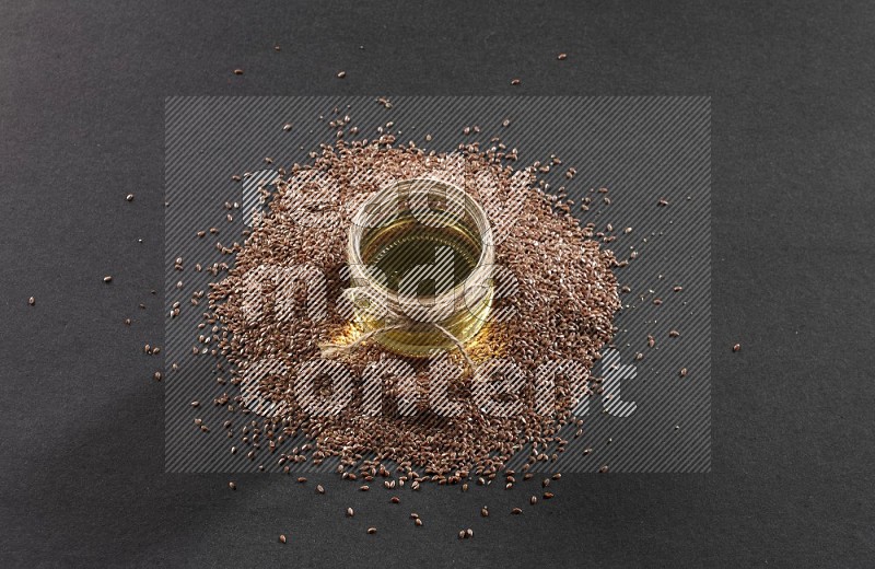 A glass jar full of flaxseeds oil surrounded by the seeds on a black flooring