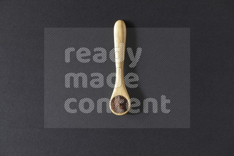 A wooden spoon full of cloves powder on a black flooring