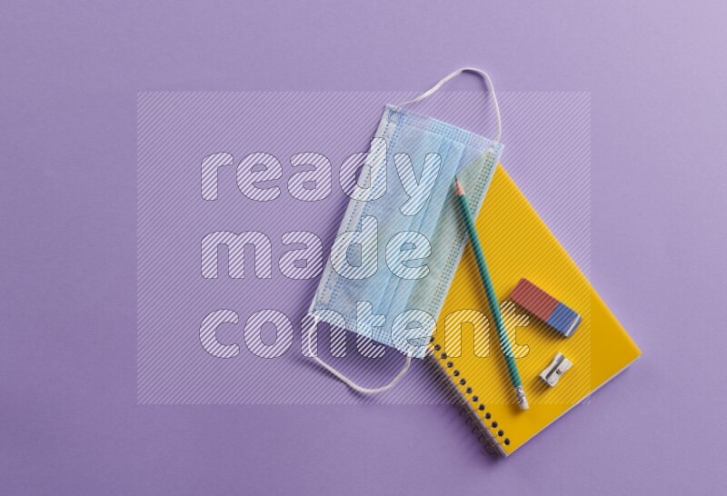A yellow notebook with school supplies on purple background