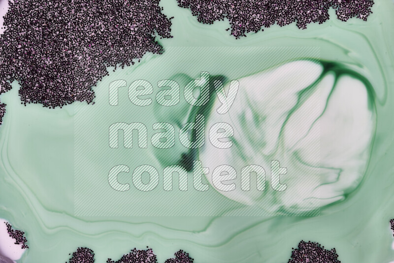 A close-up of sparkling purple glitter scattered on swirling green and white background