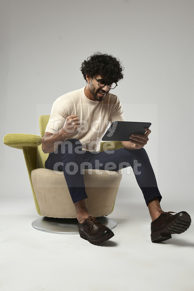 A man wearing casual sitting on a chair gaming on a tablet on white background