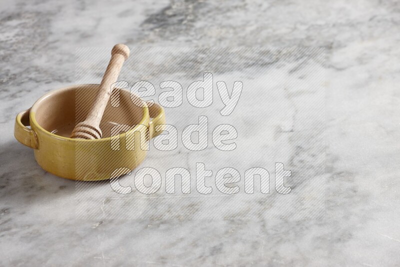 Multicolored pottery bowl with wooden honey dipper in it on grey marble background