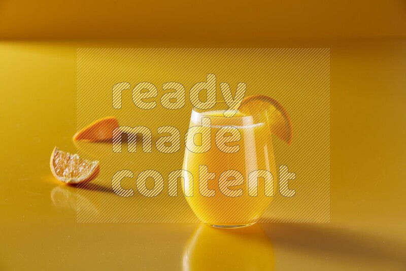 glass of orange juice with orange slice on yellow background