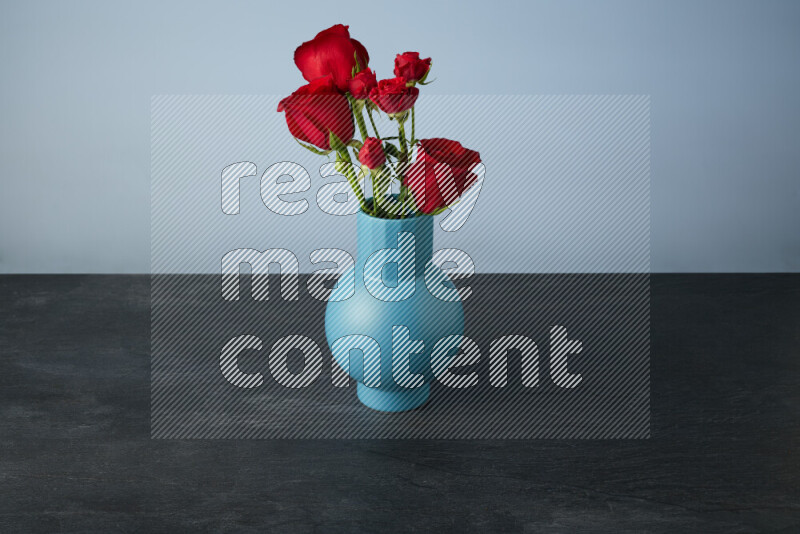 An arrangement of vivid red roses in a blue vase on black marble background