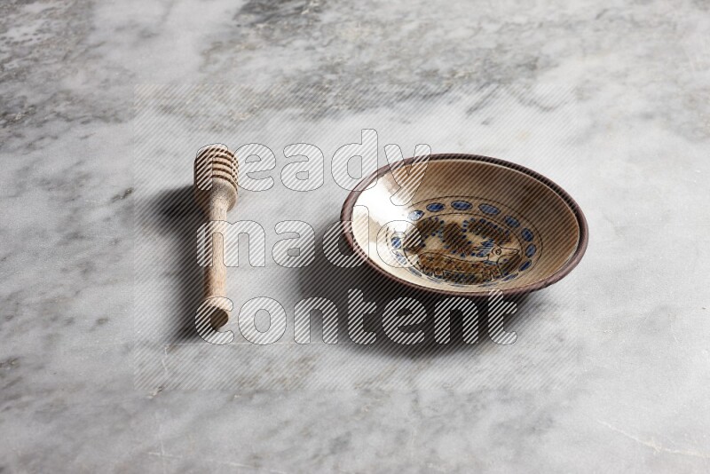 Decorative pottery plate with wooden honey dipper on the side on grey marble background