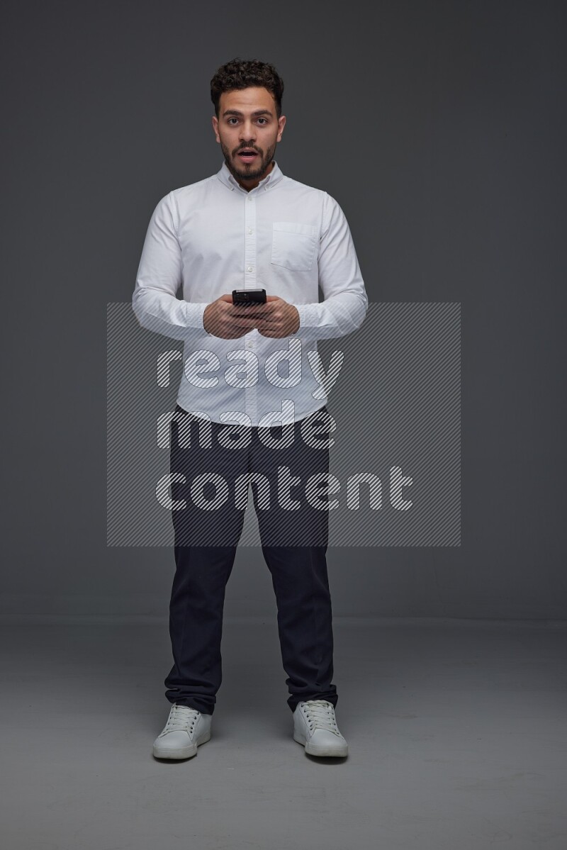 A man wearing smart casual standing and using his phone eye level on a gray background