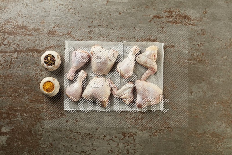 Mixed fresh chicken pieces on a parchment paper direct on a textured rustic background